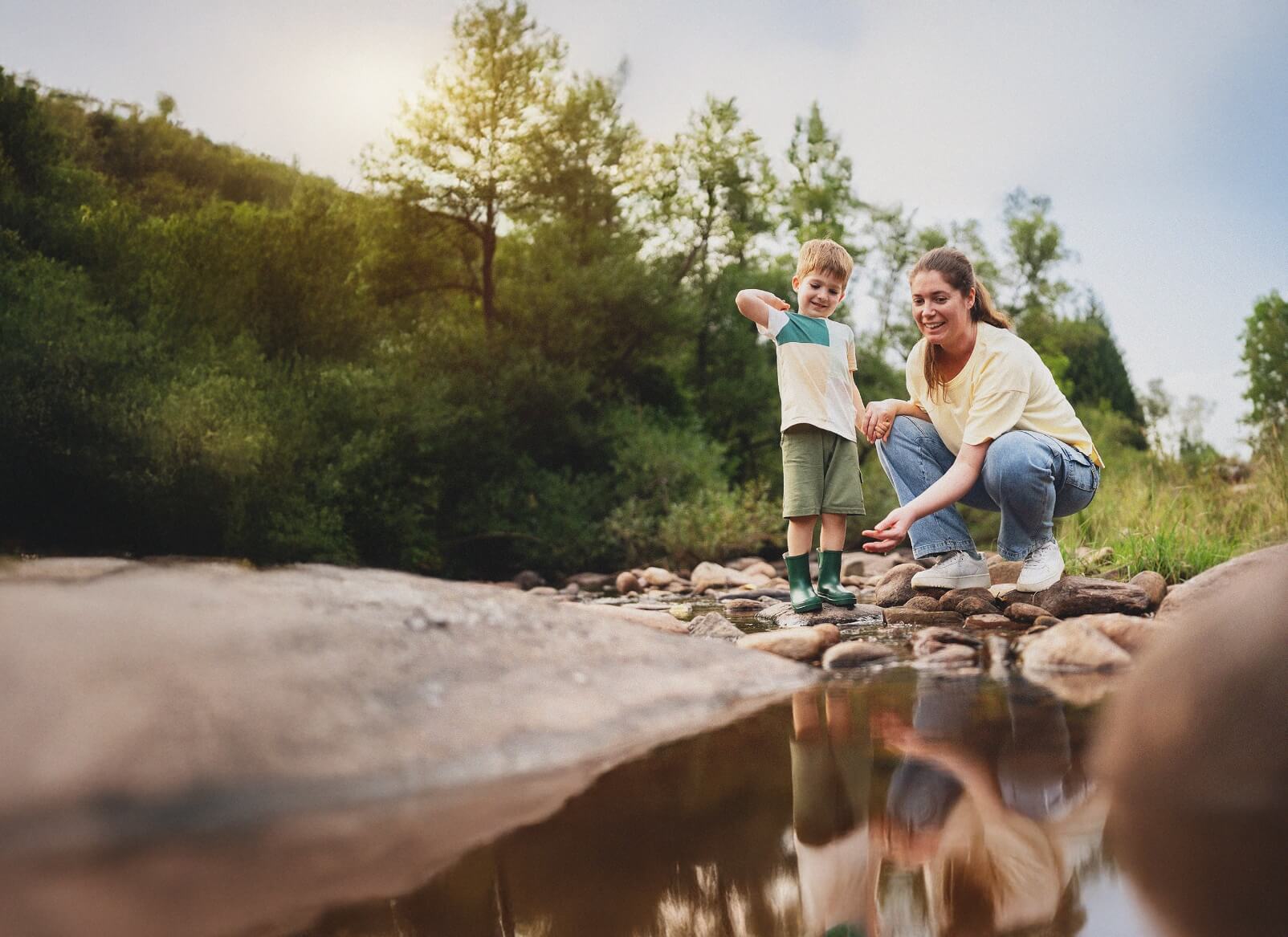 mother showing her son how to toss pebbles in a creek