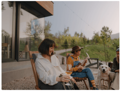 friends sit outside of their modern home in the mountains enjoying music and wine
