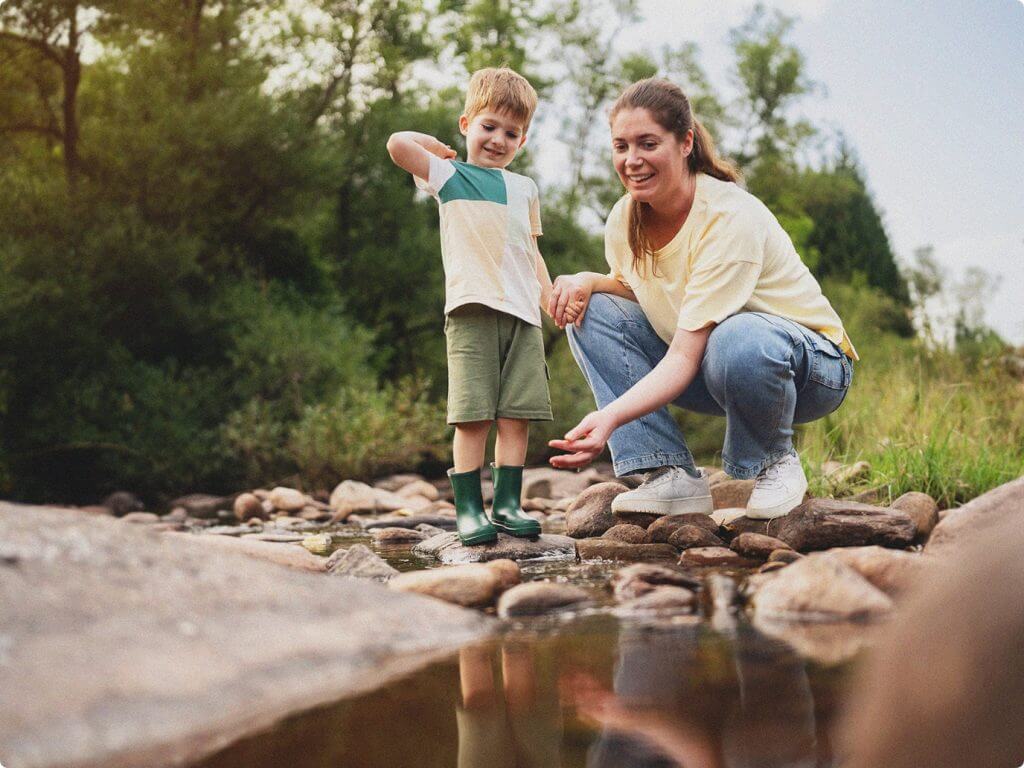 mother showing her son how to toss pebbles in a creek