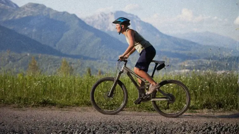A man on a mountain bike wearing sporting apparel and a helmet. He is on an outdoor trail, with the mountains in the background.