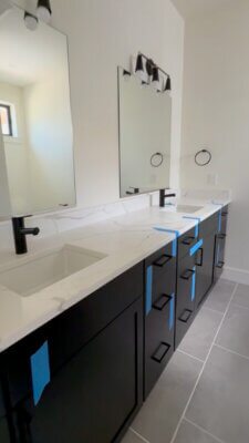 Bathroom vanity in a new Big Sky Quarry home with black cabinetry, light-colored countertops, matte black faucets, and large wall mirrors.