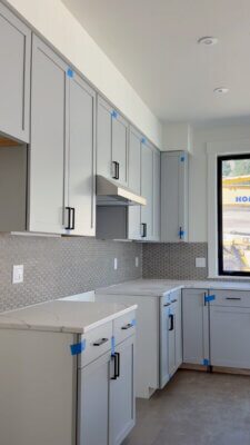Kitchen in a new Big Sky Quarry home featuring light cabinetry, black hardware, light countertops, and a gray hexagon tile backsplash.