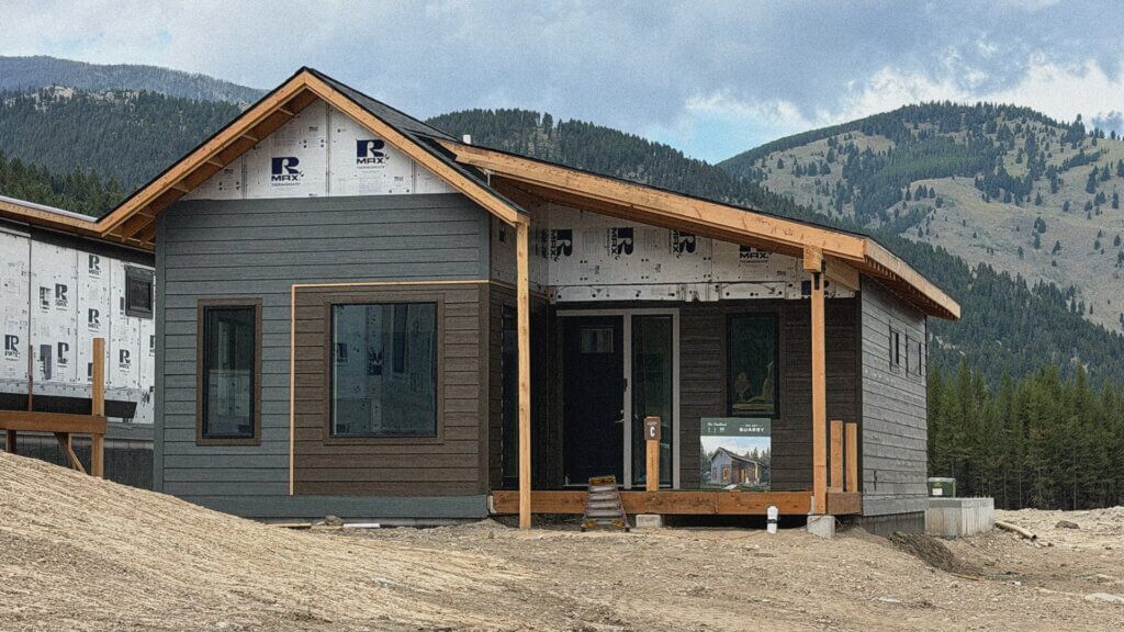 A new home with the Trailhead floor plan at Big Sky Quarry with dark wood siding, a covered front porch, and mountain views in the background.